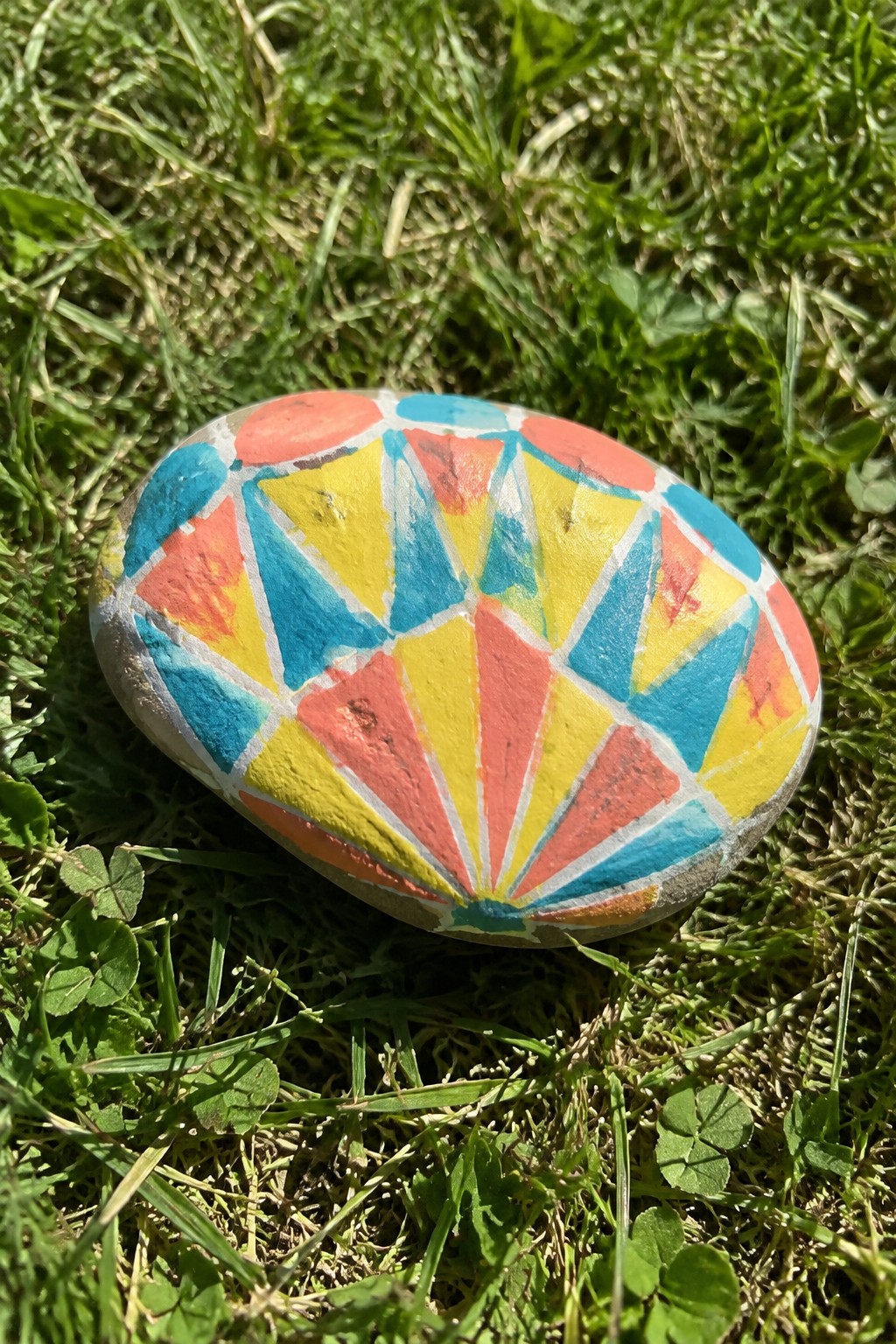 Colorful painted rock with red, yellow, blue geometric patterns on green grass.