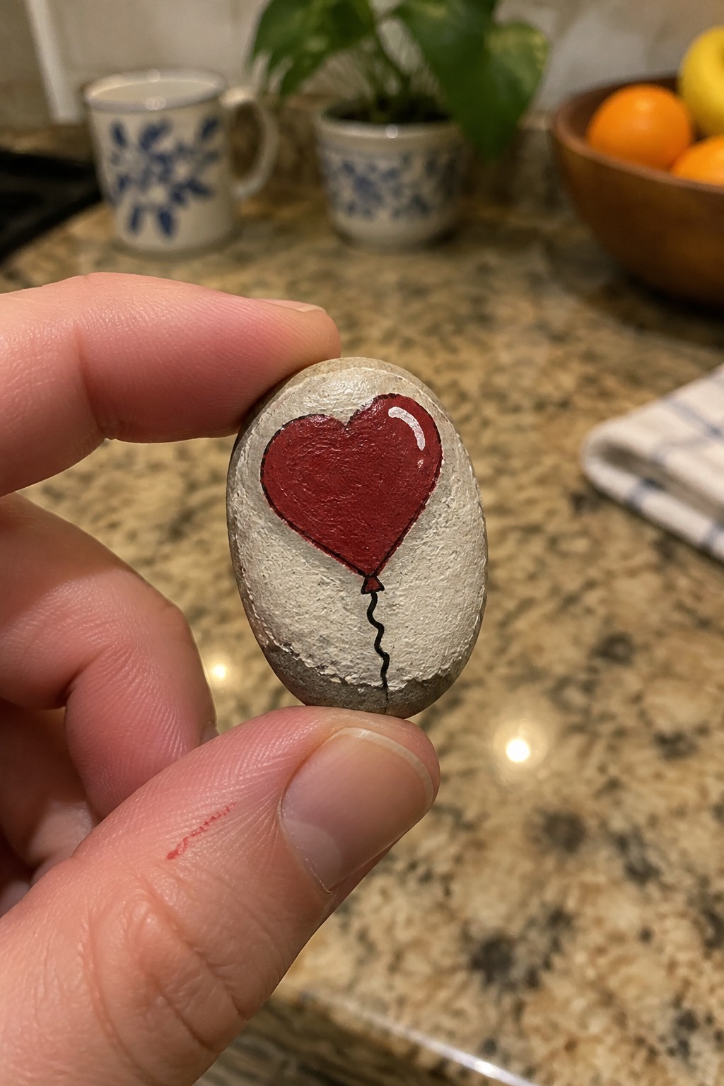 Hand holding gray stone painted with red heart balloon and string