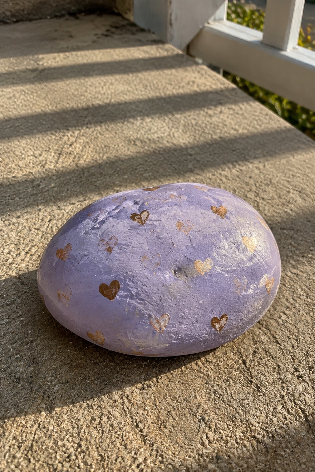 Purple rock painted with gold hearts on sunlit concrete steps