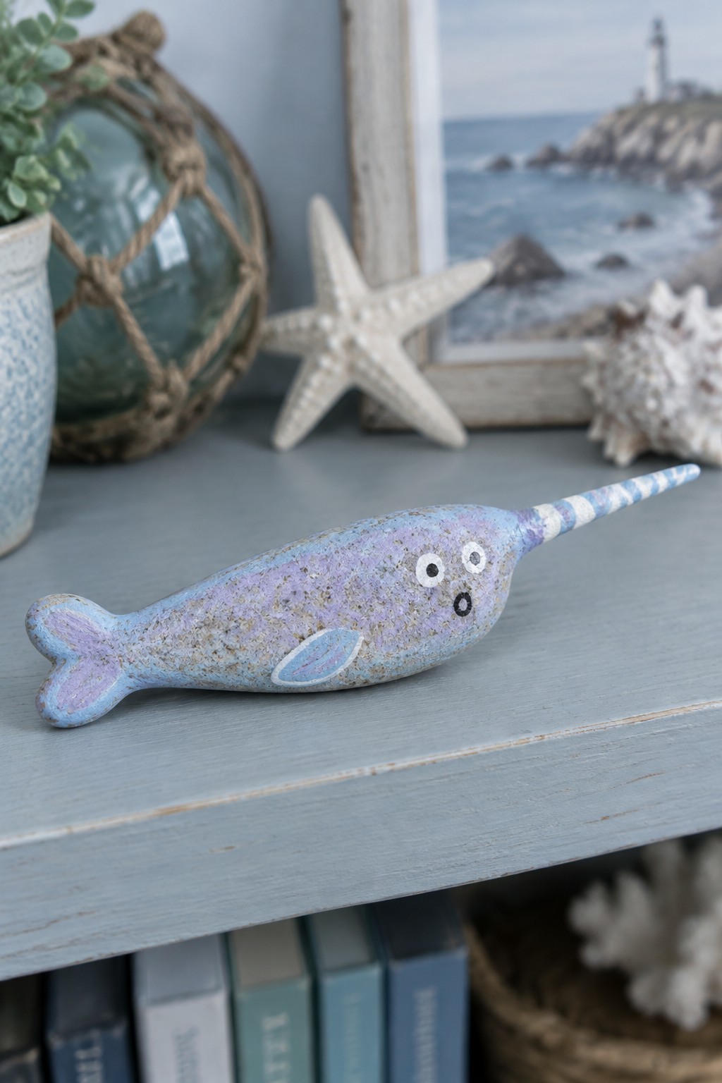 Painted blue-purple narwhal figurine with striped tusk on light blue shelf