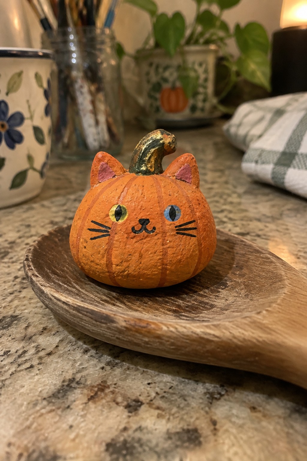 Orange cat-pumpkin figurine with painted face on wooden spoon on counter