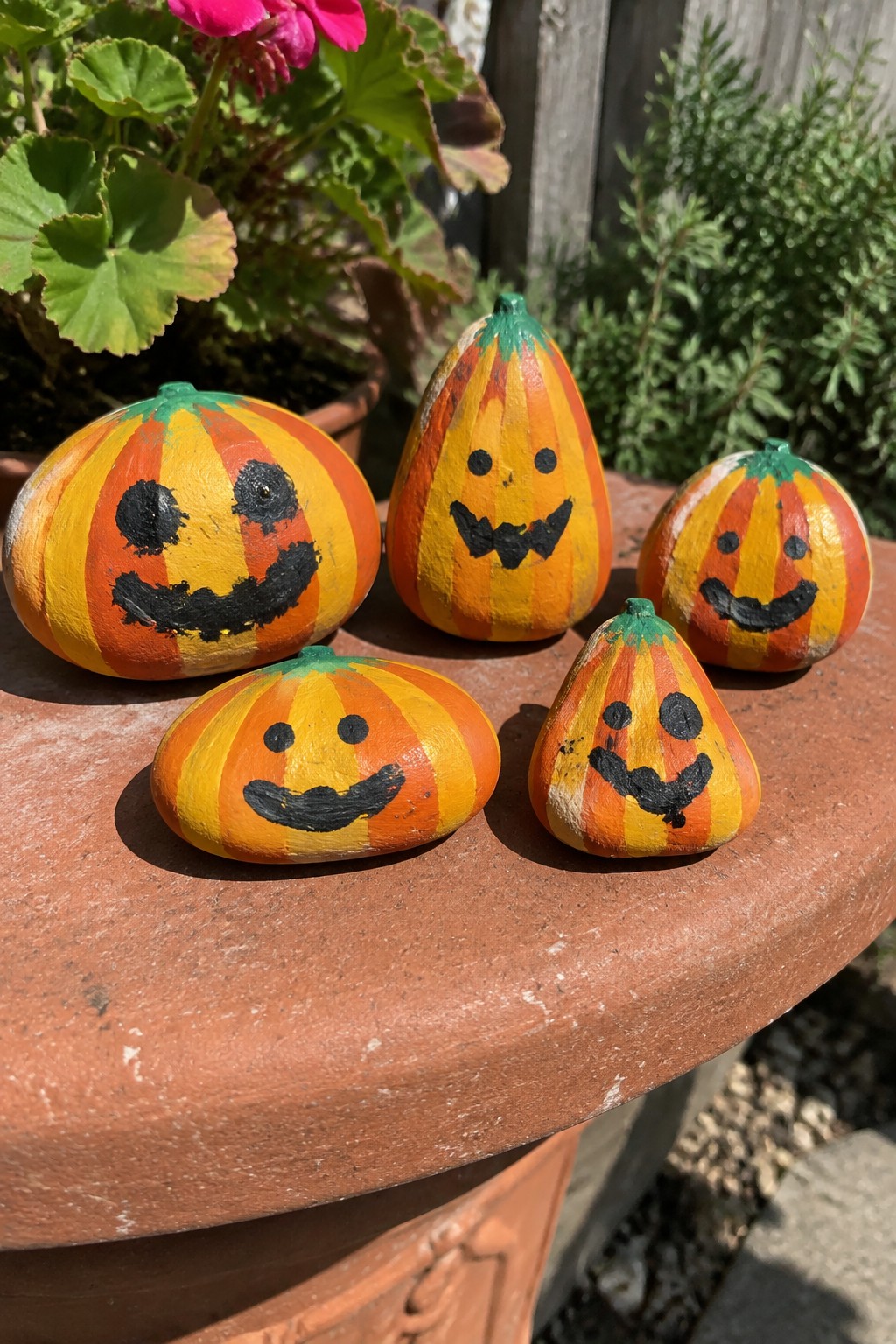 Five striped painted pumpkin rocks with jack-o'-lantern faces on a terracotta ledge.