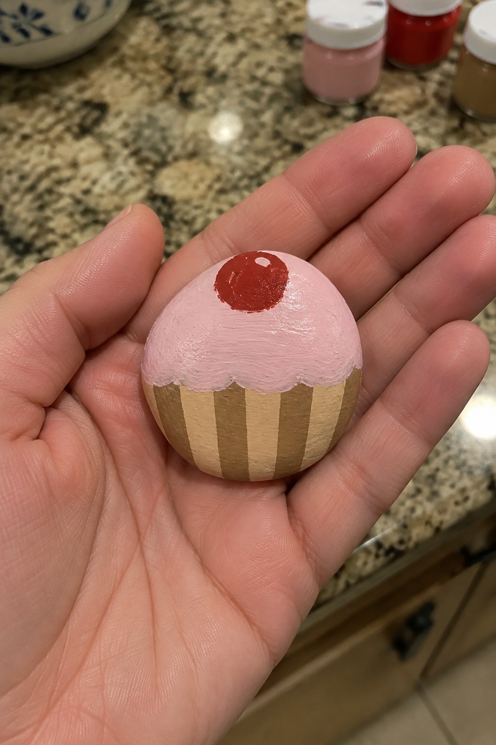 Hand holding pink painted cupcake craft with red cherry and brown stripes.