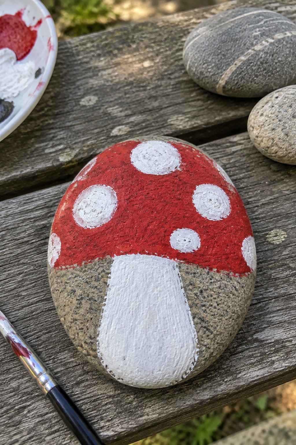 Painted mushroom rock with red spotted cap and white stem on wooden table