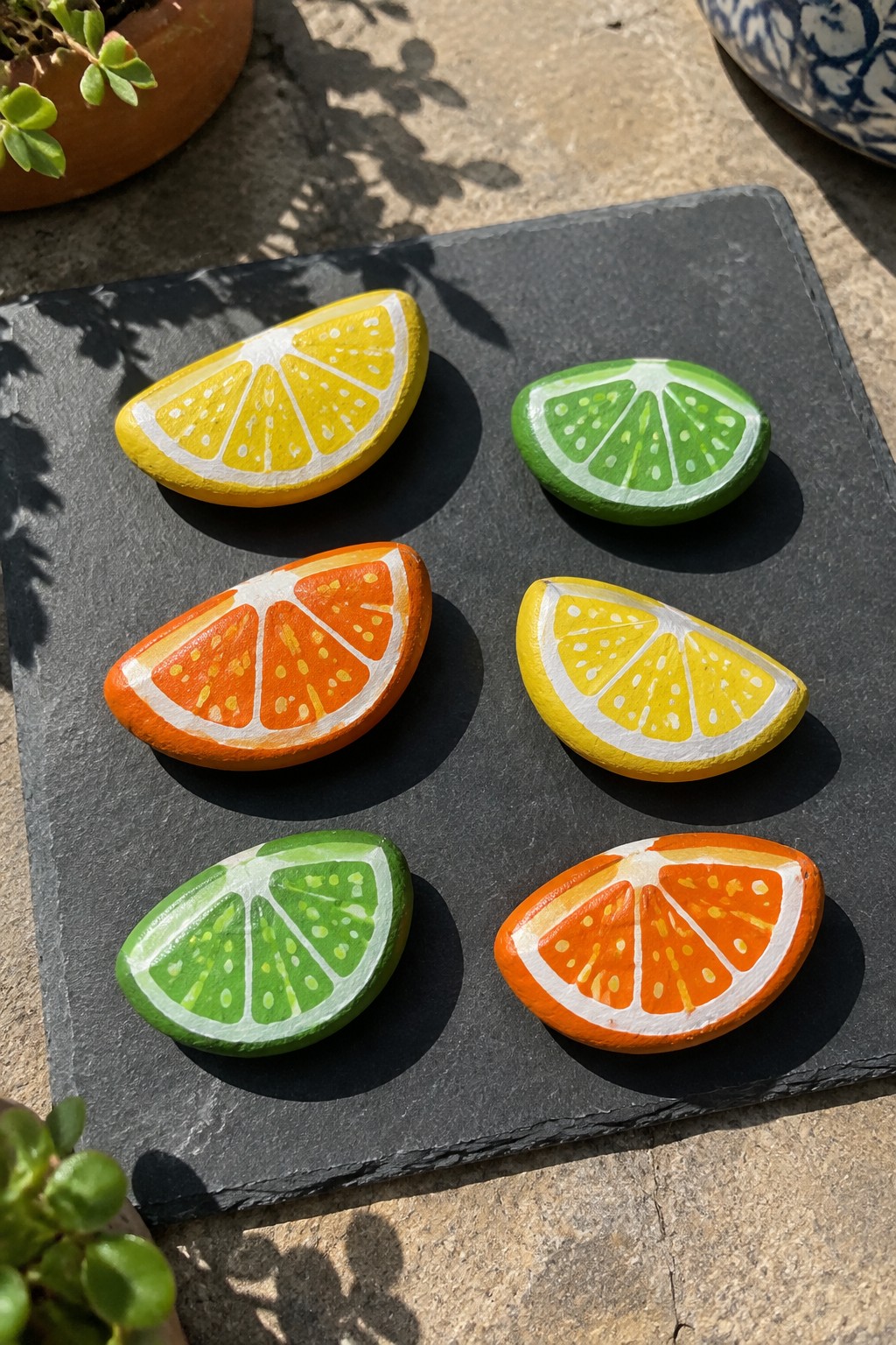 Six painted rocks as lemon, lime, and orange slices on dark slate.