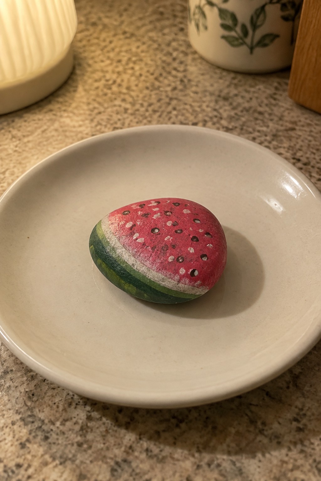 Watermelon-painted rock with black seeds on a white plate on countertop