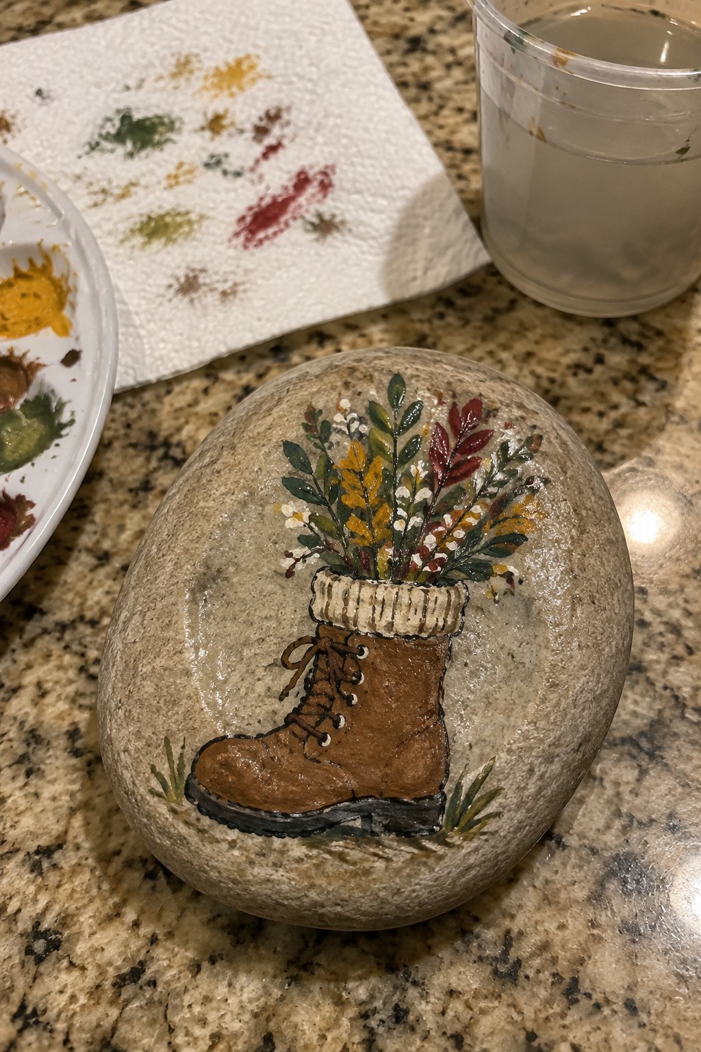 Painted rock with brown lace-up boot and knitted cuff filled with autumn leaves and flowers