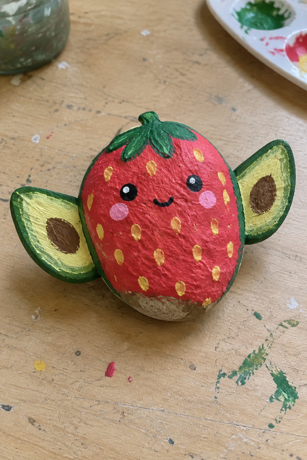Painted strawberry with smiling face and avocado wings on wooden table.
