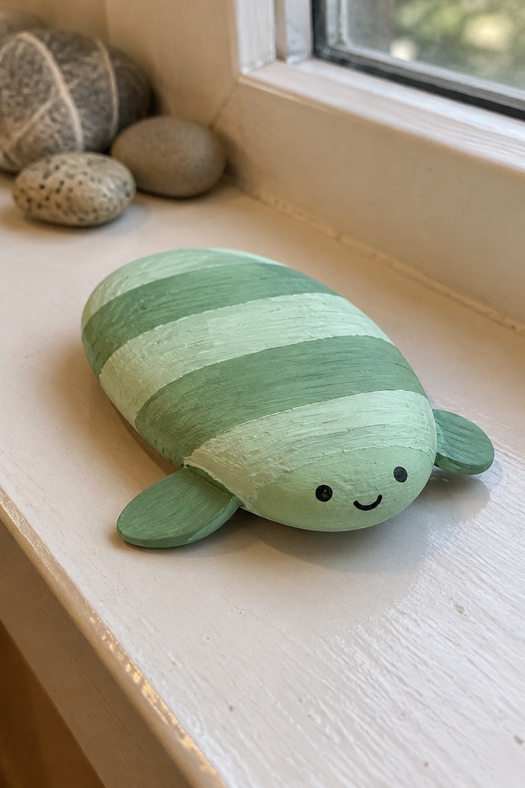 Green striped painted turtle rock with smiling face on white windowsill