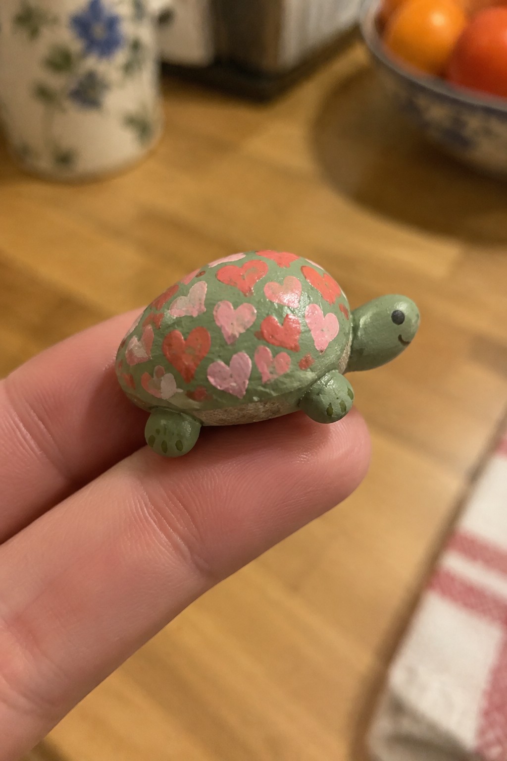 Hand holding small green turtle figurine with pink and red heart-patterned shell