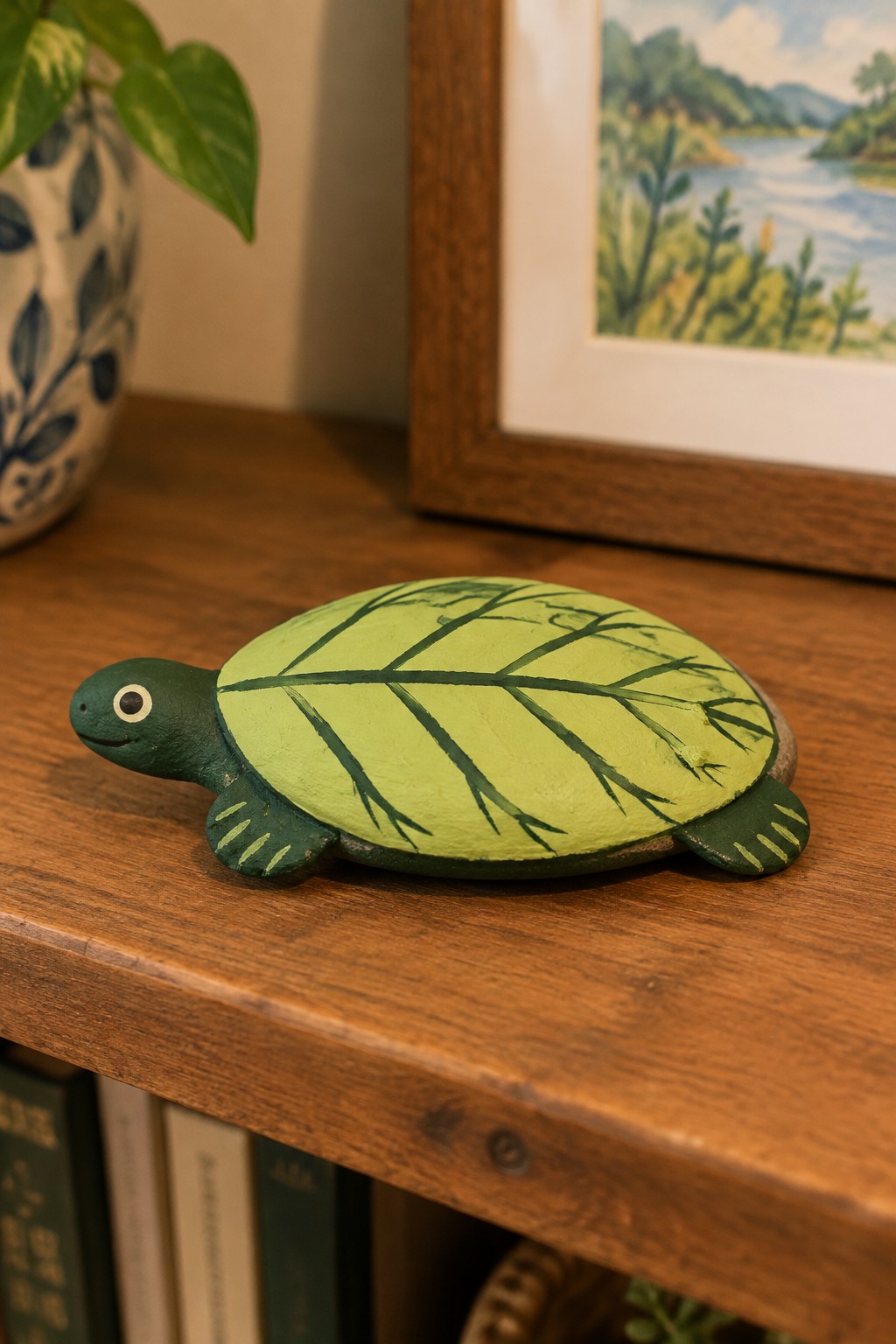 Green wooden turtle figurine with leaf-patterned shell on a wooden shelf.