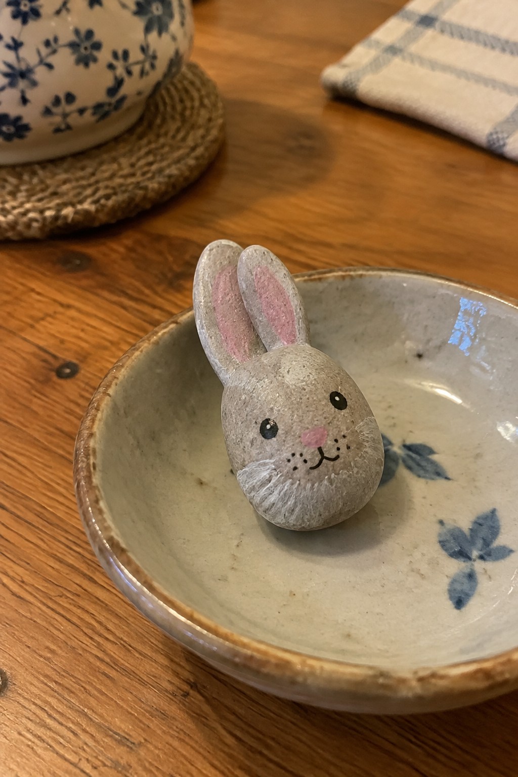 Gray painted bunny rock with pink ears in ceramic bowl on wooden table