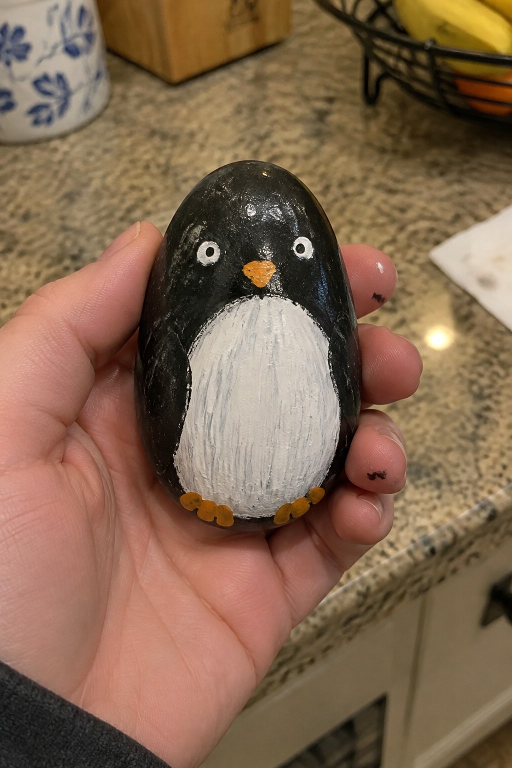 Hand holding painted rock penguin with black body, white belly, orange beak and feet