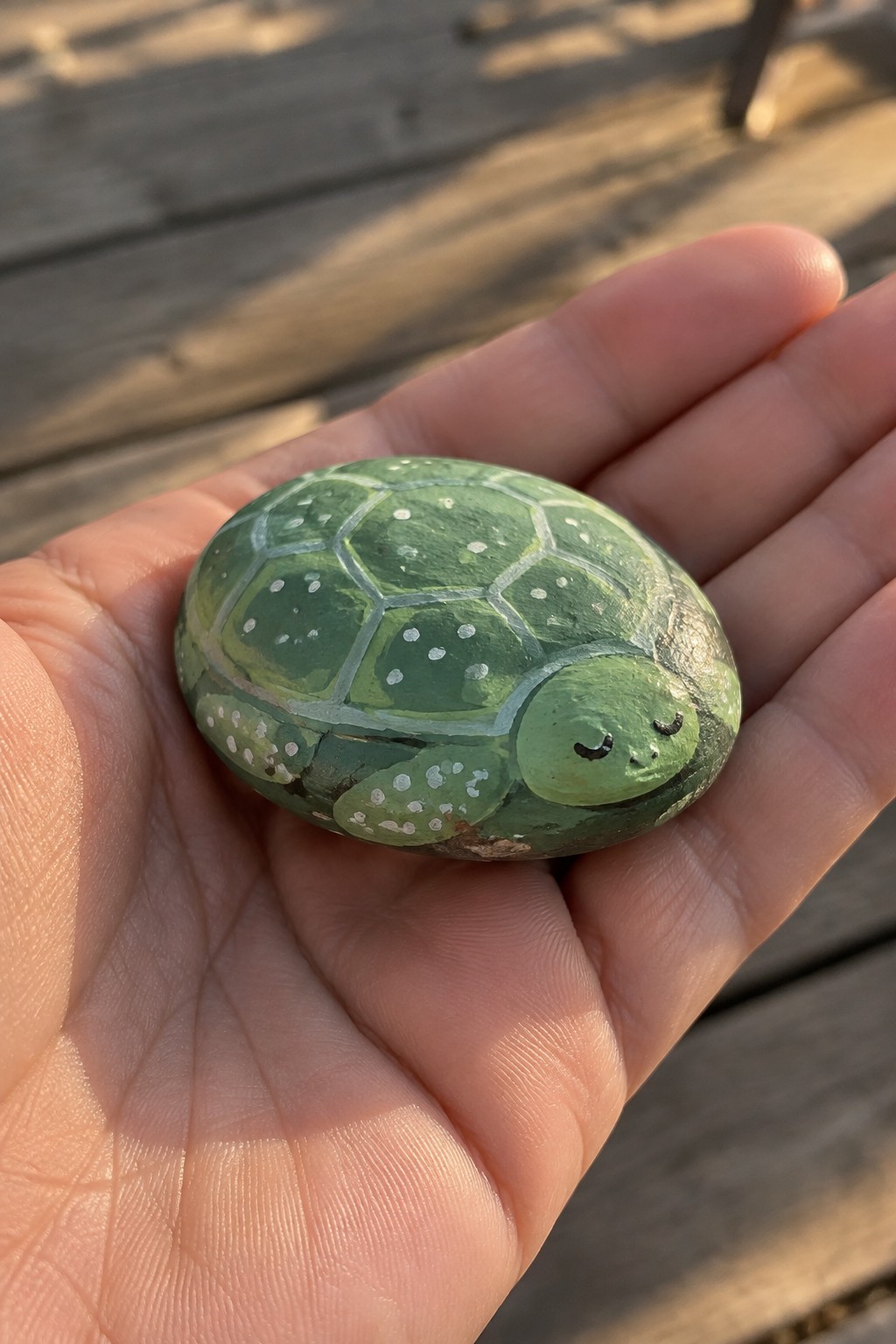 Hand holding green painted rock turtle with hexagonal shell, white dots, and smiling face.