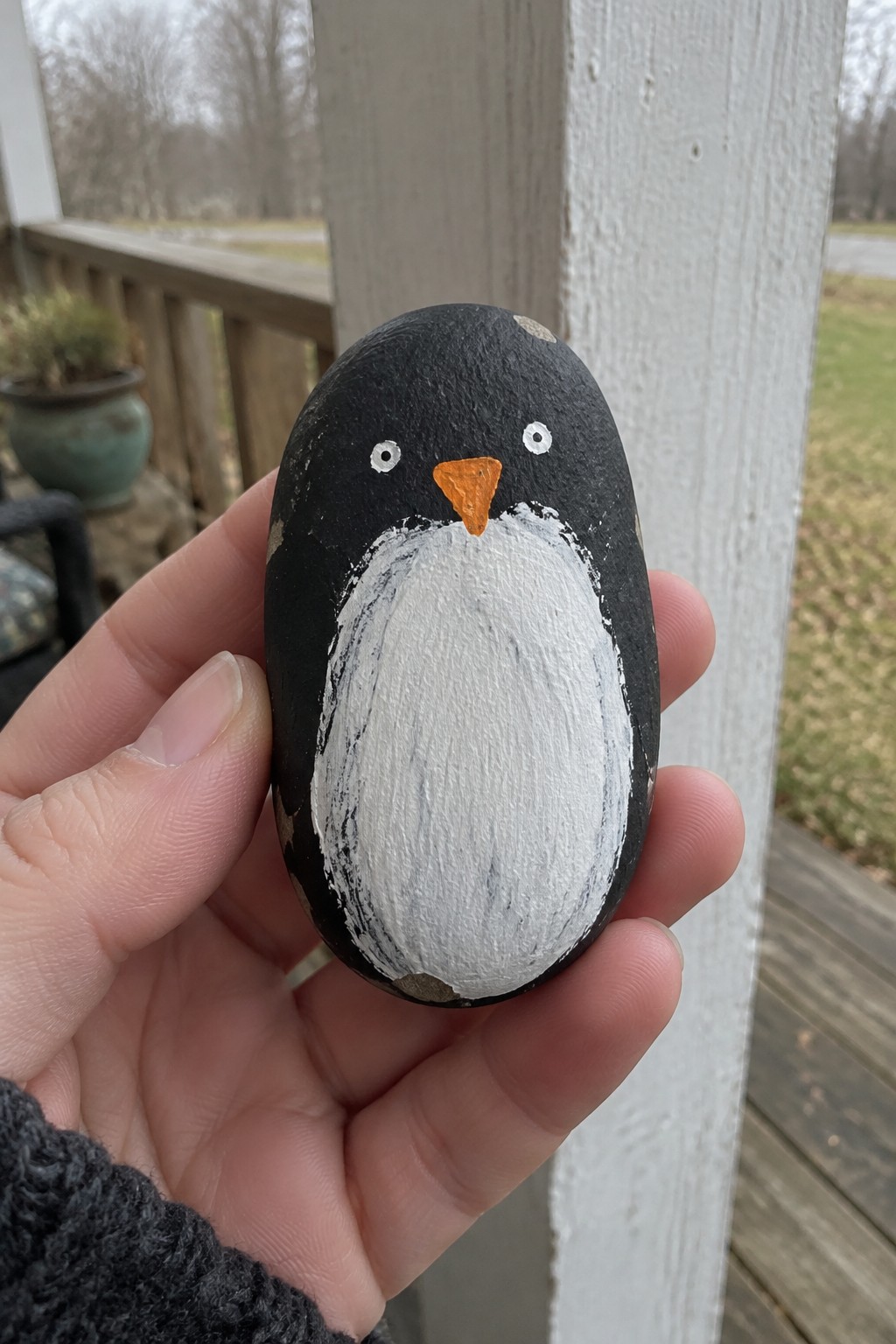 Hand holding oval rock painted as penguin with white belly and orange beak