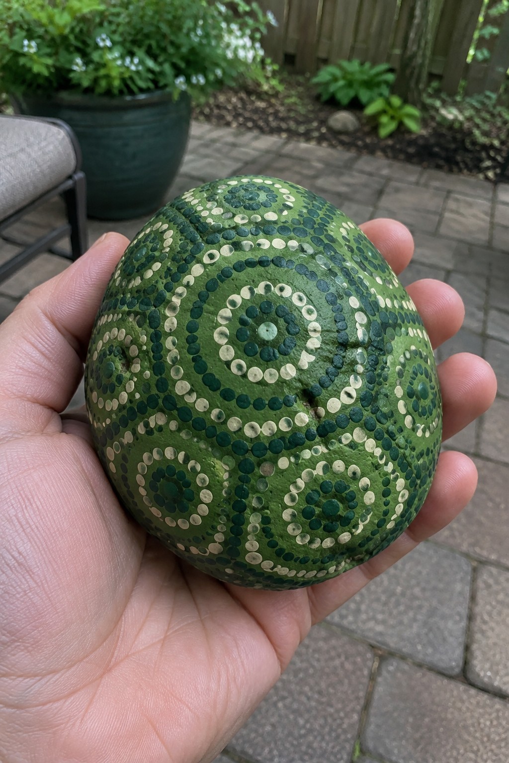 Hand holding green painted rock with concentric white and dark green dot patterns