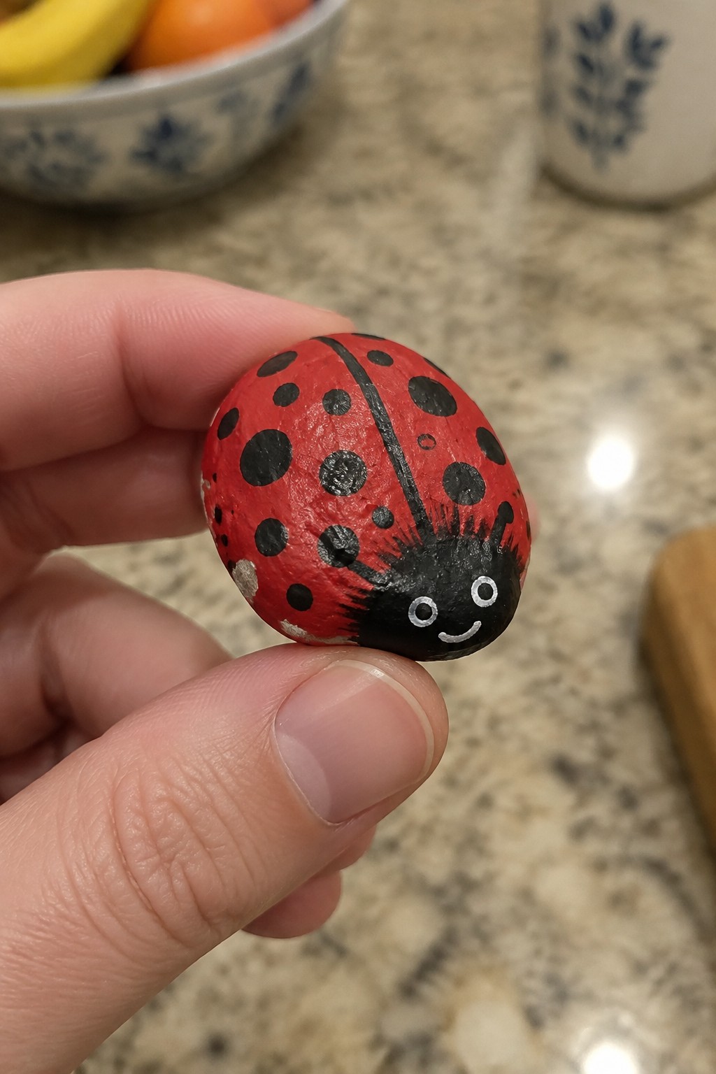 Hand holding red painted ladybug rock with black spots and smiling face