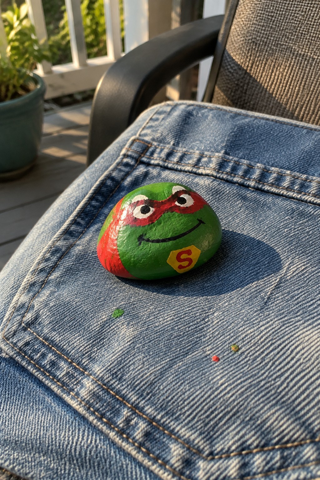 Green painted turtle rock with red mask on blue denim jeans