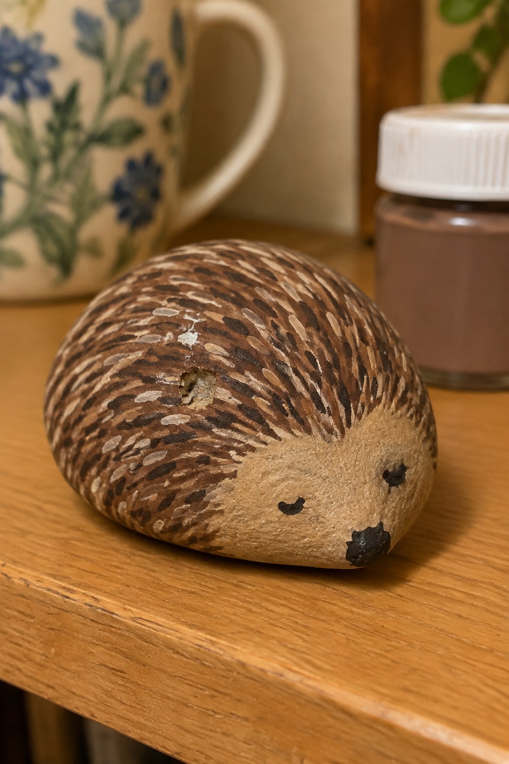 Painted hedgehog rock with brown spines and black face on wooden table.