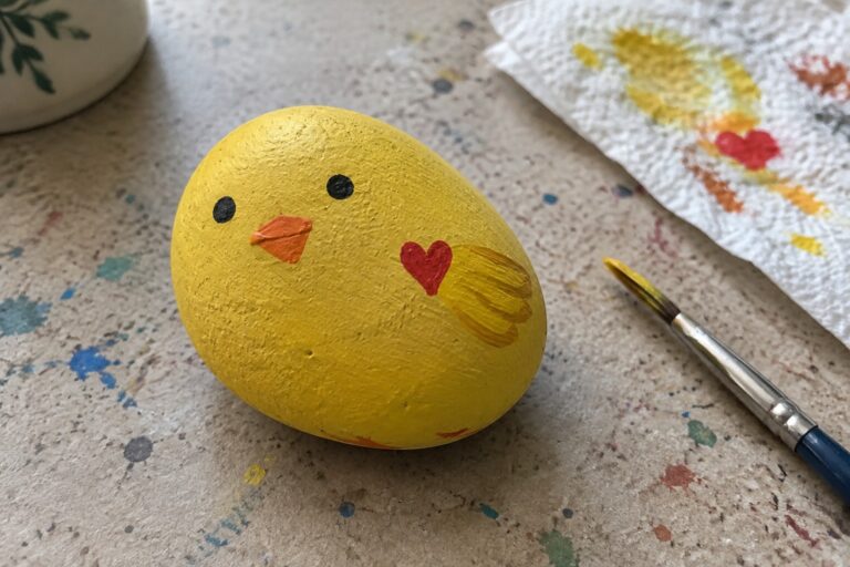 23 Funny and Inspirational Painted Rocks With Expressive Faces and Short Messages Yellow chick rock with black eyes, orange beak, red heart beside paintbrush